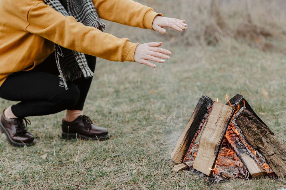 Person warming hands by a DIY campfire in a natural setting, emphasizing outdoor comfort and fire pit enjoyment.