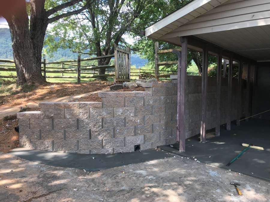 Block retaining wall under construction near a shaded outdoor area, highlighting expert masonry services in Etowah, NC, designed for durable and aesthetic landscaping solutions.