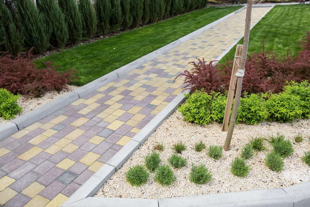 Paved walkway with colorful stone patterns surrounded by lush green grass, decorative shrubs, and fresh landscaping, illustrating custom outdoor design by Laughter Family Hardscapes for Asheville homeowners.