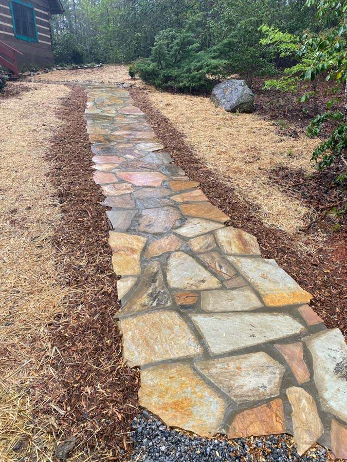 Natural stone pathway leading through landscaped yard with mulch and greenery, showcasing hardscaping by Laughter Family Hardscapes in Asheville, NC.