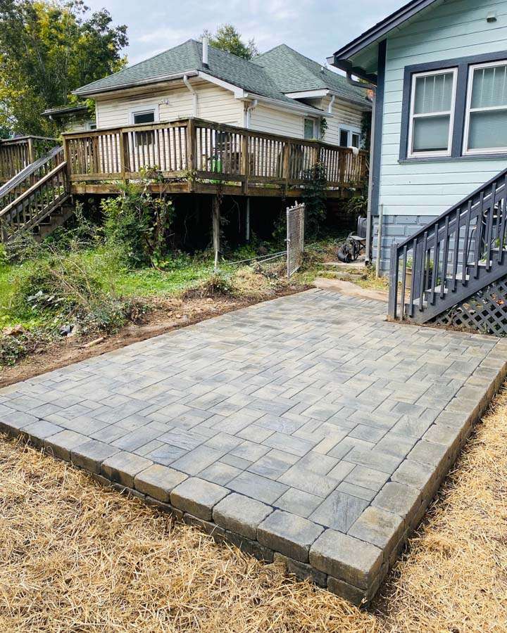 Paved stone patio installation by Laughter Family Hardscapes, showcasing custom hardscaping in Asheville, NC, with adjacent house and landscaping elements.
