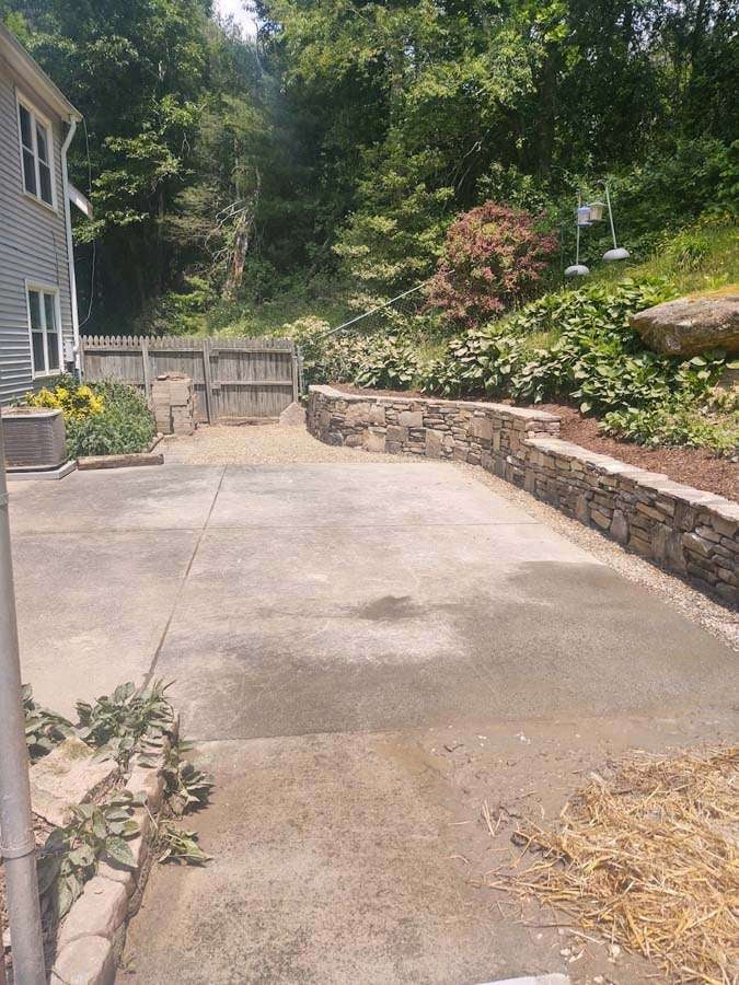 Hardscaped outdoor area featuring a stone retaining wall, concrete surface, and landscaped surroundings with greenery, showcasing Laughter Family Hardscapes' custom landscaping services in Asheville, NC.