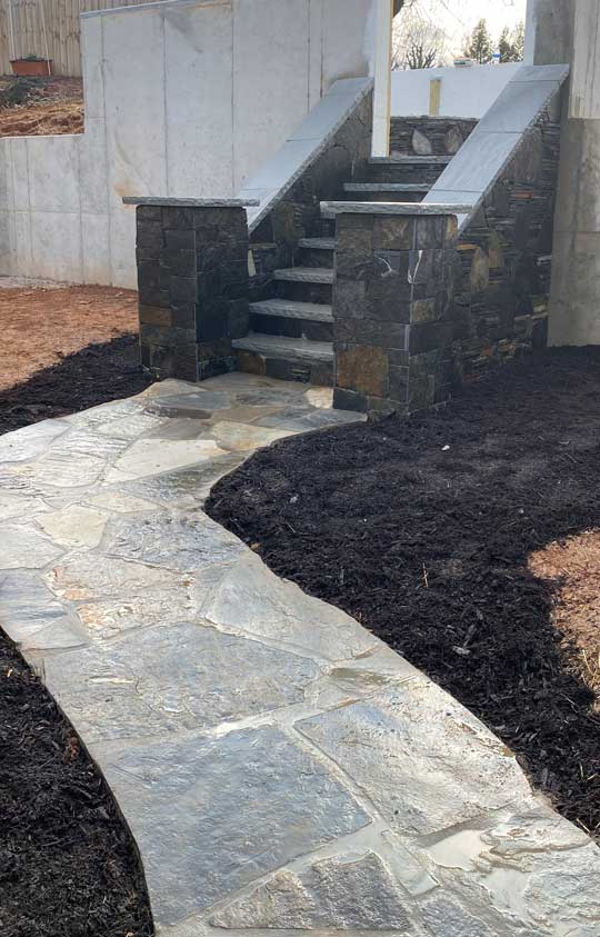 A beautifully crafted stone walkway leading to a set of sturdy stone stairs with masonry pillars, highlighting expert masonry services in Etowah, NC.