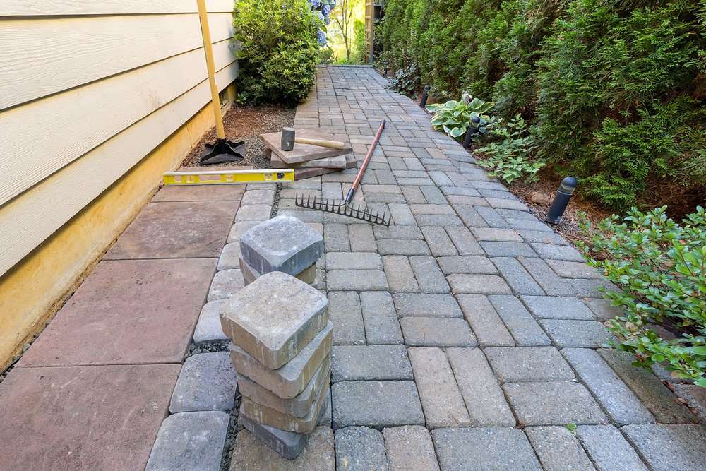 Paver pathway installation with stacked pavers and landscaping tools, showcasing hardscaping options for enhancing outdoor spaces.