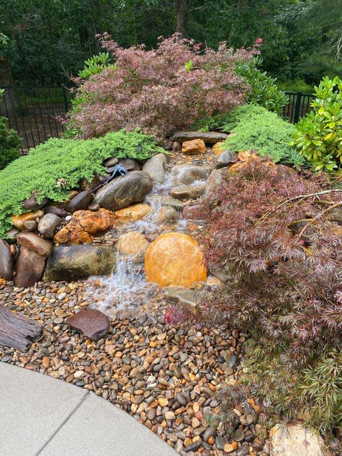 Water feature with natural stones, colorful foliage, and pebbled landscaping, enhancing outdoor space design by Laughter Family Hardscapes in Etowah, NC.