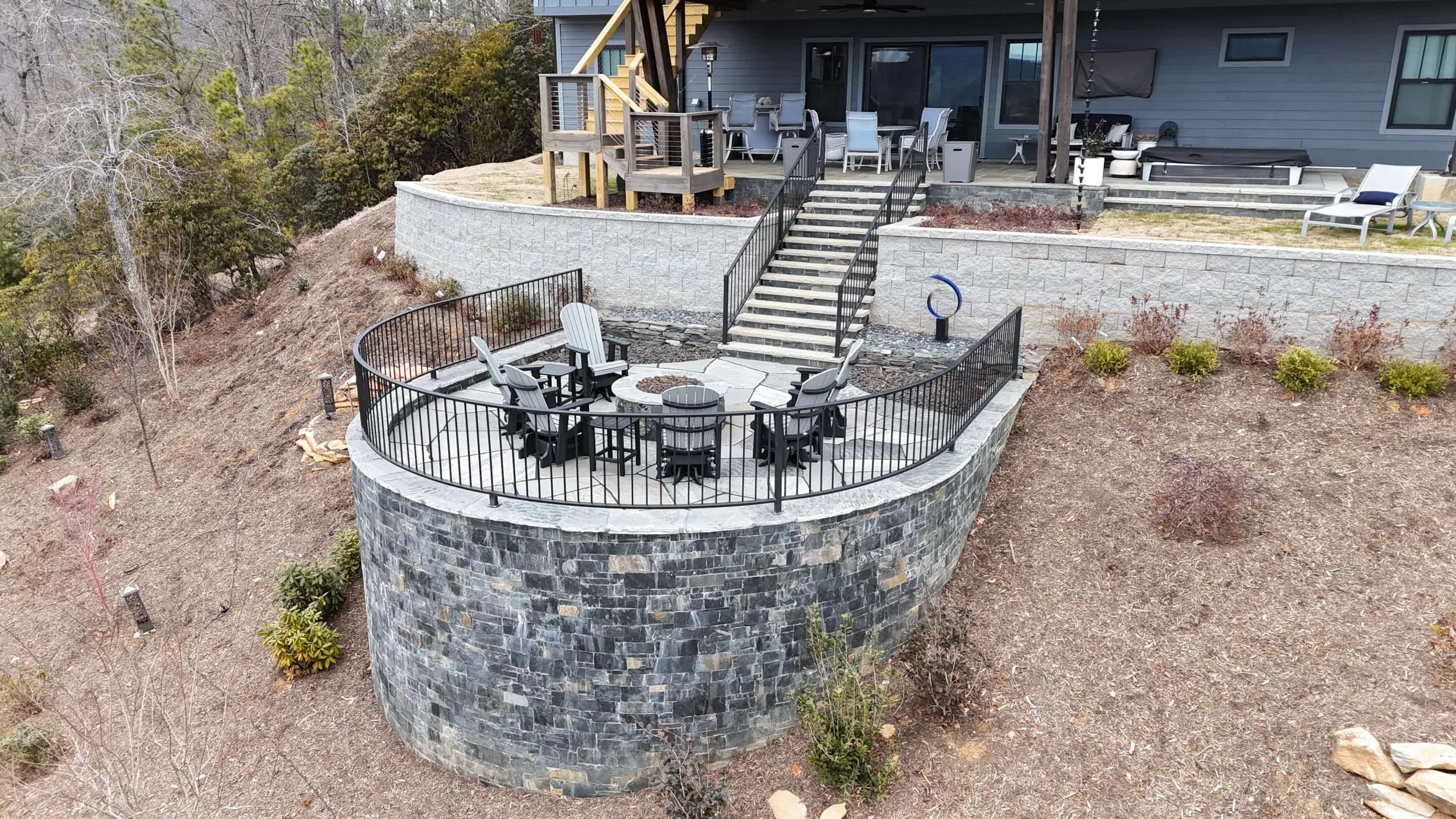 Outdoor hardscaping featuring a circular stone patio with black metal railing, surrounded by landscaping, adjacent to a modern home in Etowah, NC, showcasing Laughter Family Hardscapes' design expertise.