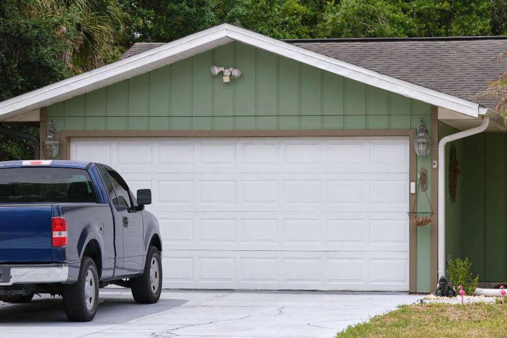 Vehicle parked in front of a wide, white garage double door, showcasing a well-maintained driveway and residential landscaping, relating to driveway design and maintenance tips.