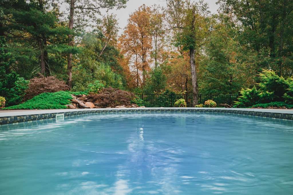 Custom hardscaping project featuring a serene swimming pool surrounded by lush greenery and autumn foliage, showcasing Laughter Family Hardscapes' landscaping expertise in Asheville, NC.