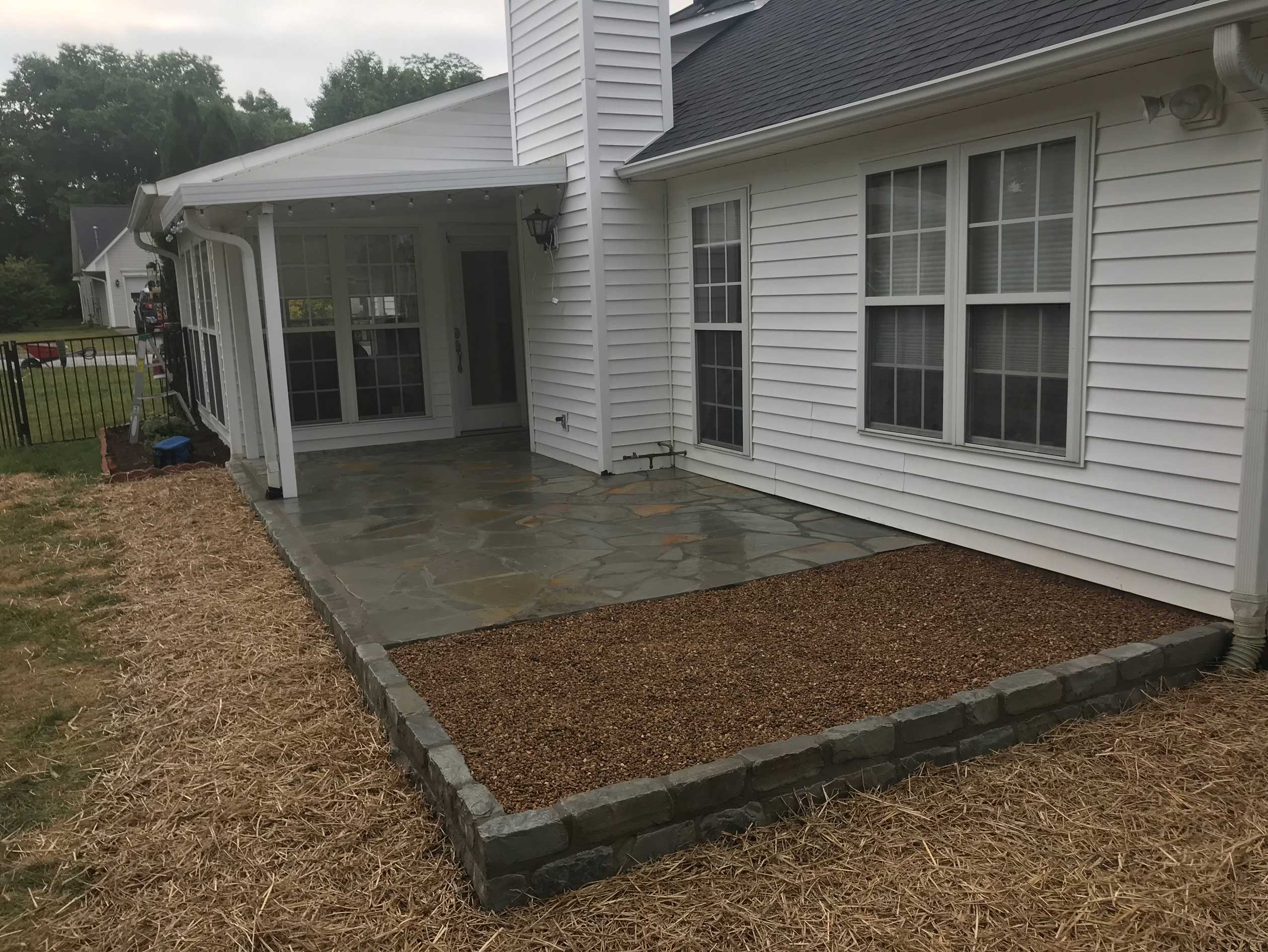 A professionally designed backyard featuring a sleek flagstone patio bordered by a gravel walkway and straw-covered landscaping, showcasing expert hardscaping services in Etowah, NC.