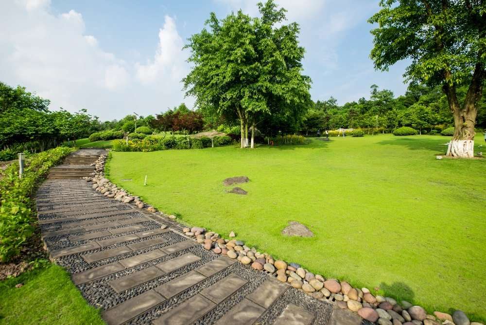 A beautifully landscaped park in Etowah, NC, featuring a paved walkway lined with decorative stones, lush green grass, vibrant trees, and well-maintained shrubbery, showcasing expert landscaping services in the area.