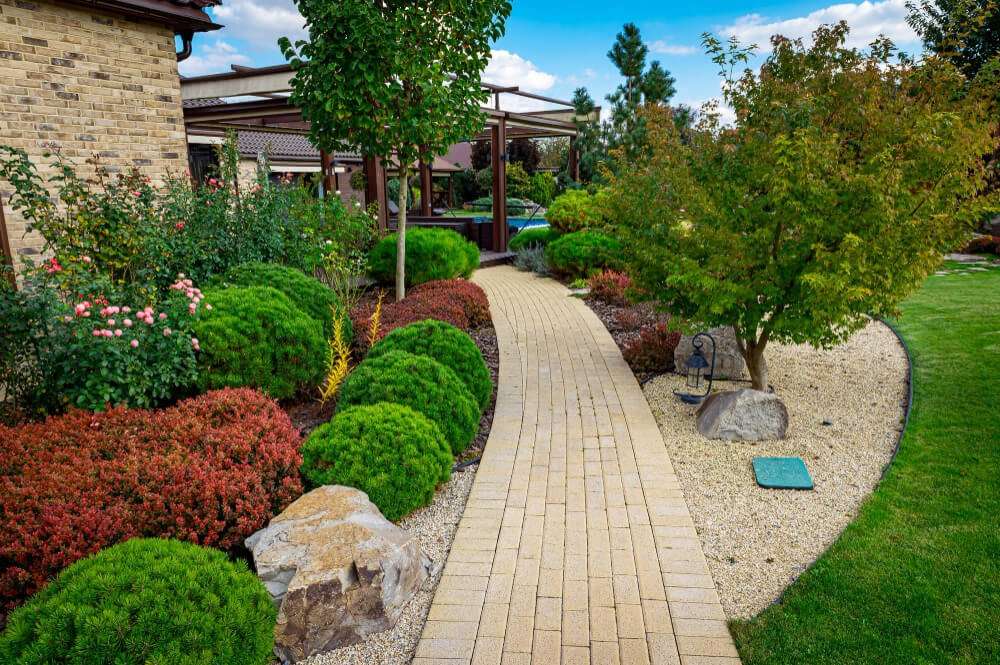 Flagstone walkway meandering through a landscaped garden with vibrant shrubs and decorative stones, enhancing outdoor living spaces in Etowah, NC.