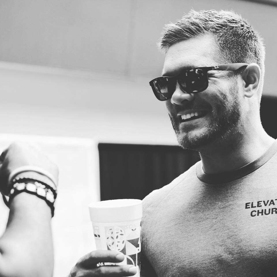 A smiling member of the hardscaping team in Etowah, NC, wearing sunglasses and holding a drink, representing Laughter Family Hardscapes.