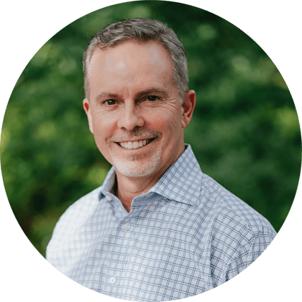 Smiling man in a checkered shirt against a green background, representing client satisfaction for Laughter Family Hardscapes landscaping services.