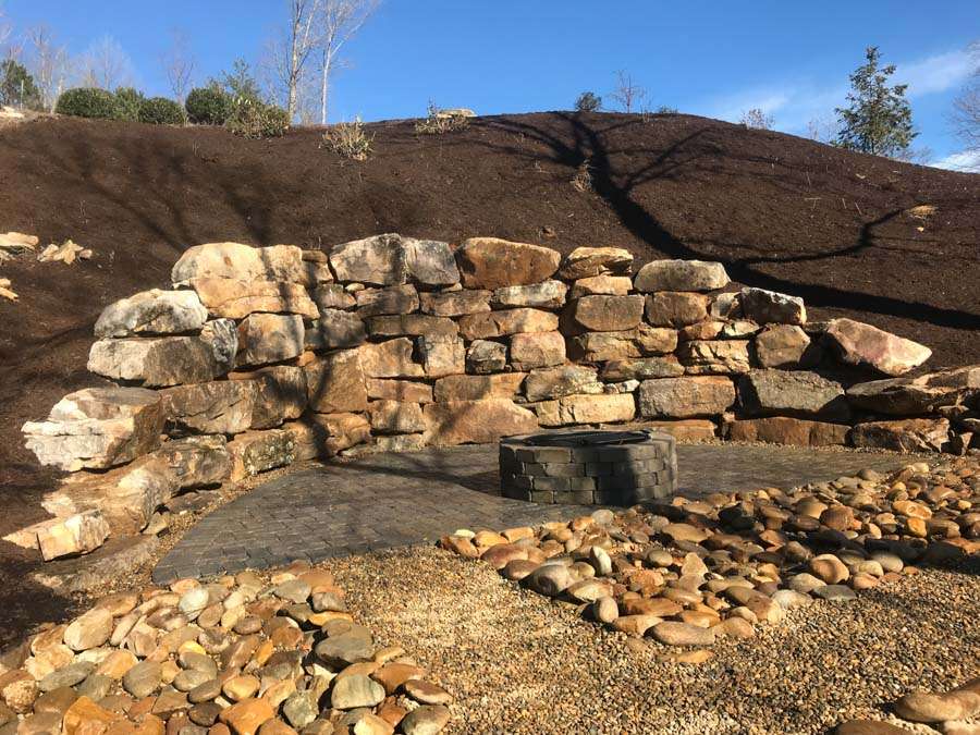 Natural stone retaining wall with a built-in fire pit and surrounding paver patio, showcasing premium masonry services in Etowah, NC, designed for functional and rustic outdoor living spaces.