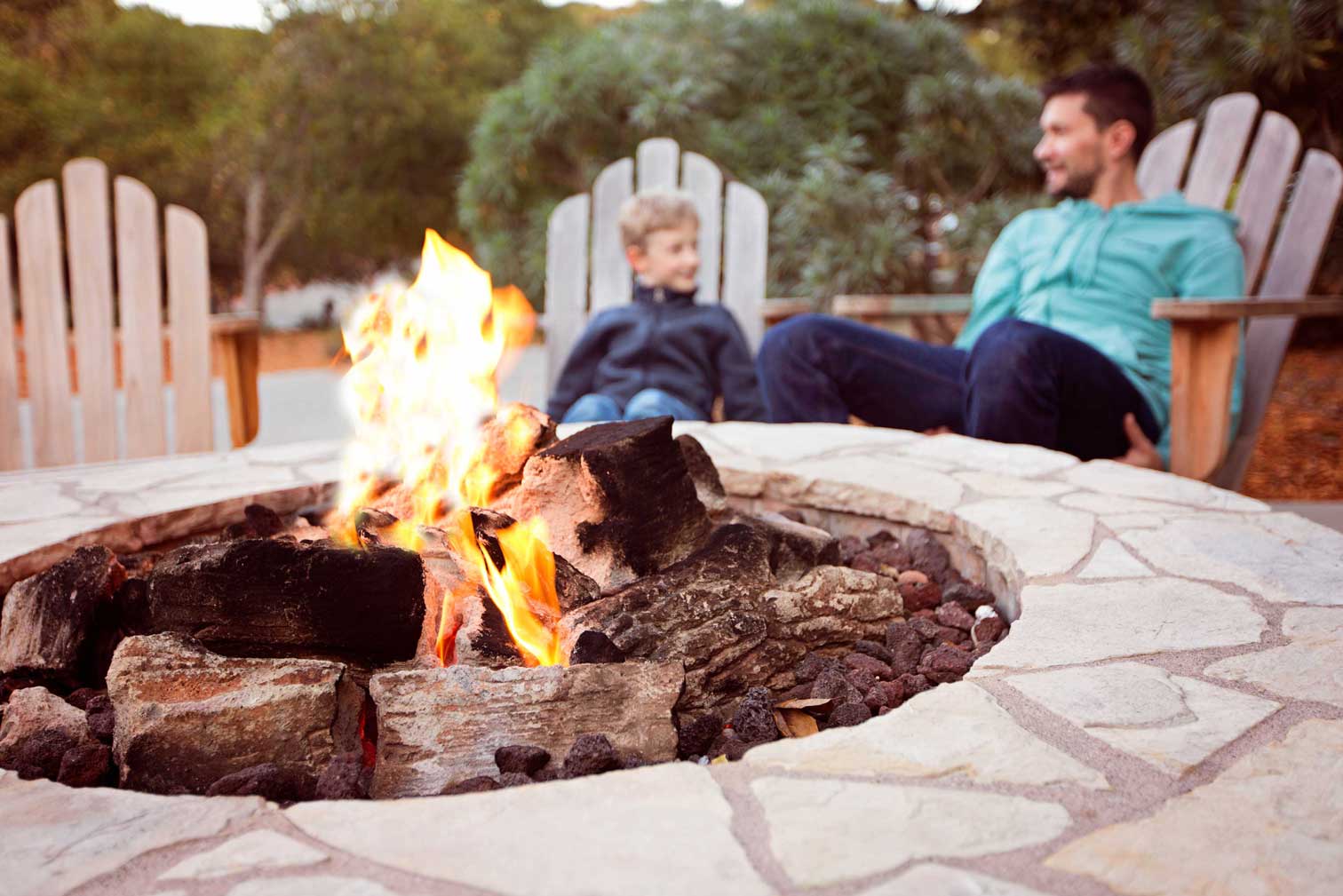 Stone fire pit with vibrant flames surrounded by Adirondack chairs, offering a cozy outdoor gathering spot, showcasing professional masonry services in Etowah, NC.