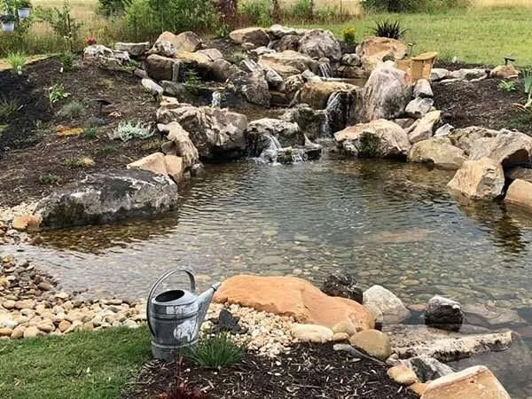 Serene landscape design featuring a natural stone pond with cascading water, surrounded by rocks and greenery, showcasing Laughter Family Hardscapes' expertise in hardscaping and outdoor space creation.