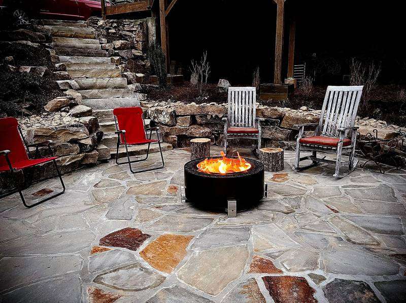 Outdoor firepit surrounded by red and white chairs on a stone patio, enhancing outdoor kitchen ambiance and social gatherings.
