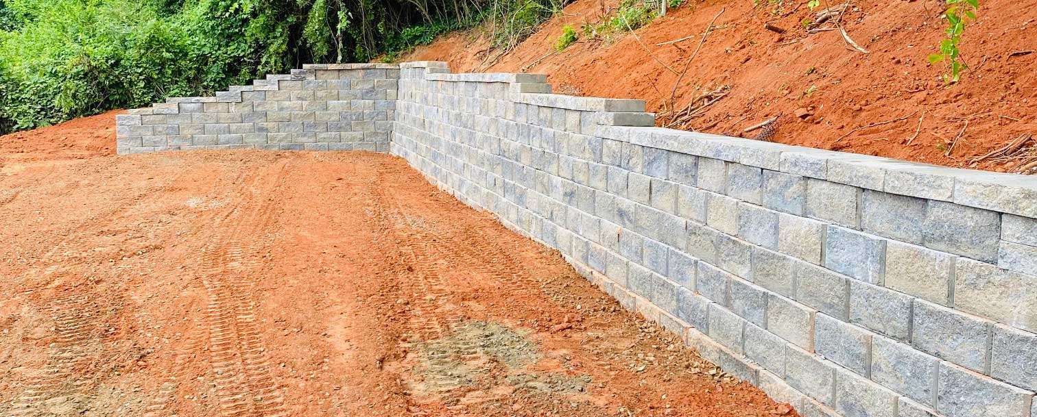 Segmental block retaining wall under construction beside an excavated slope